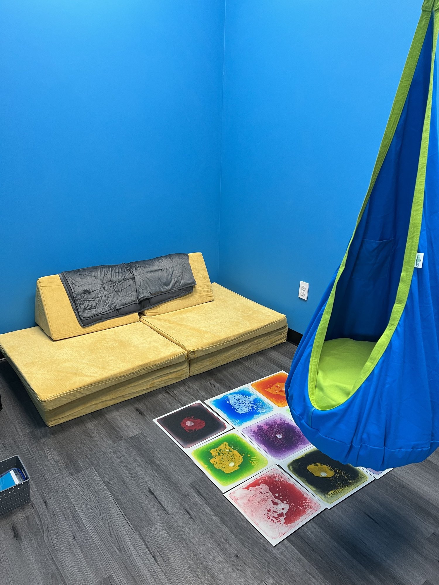 Blue Sensory Room with couch, weighted blanket, floor tiles, swing hook, fidget toys, light feature, and calm down kit 